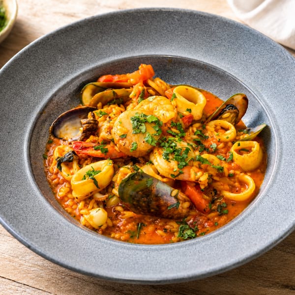 Seafood stew with prawns, squid, mussels, and rice in a rich tomato sauce, garnished with fresh herbs.