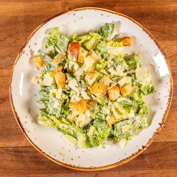 A fresh Caesar salad with crisp romaine lettuce, croutons, and parmesan cheese on a white plate.