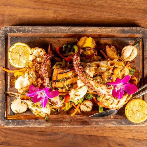 Grilled seafood platter with octopus, shrimp, scallops, fish, vegetables, and lemon, garnished with orchids.