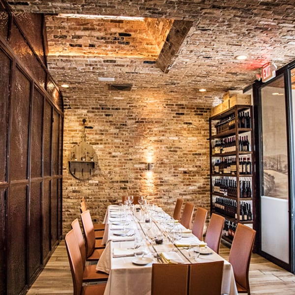 Private dining room with a long set table, exposed brick, and shelves of wine bottles.