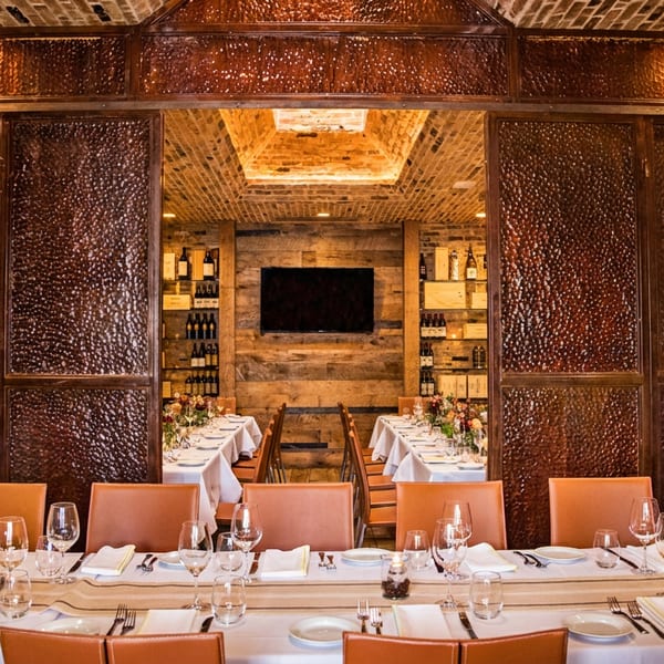 Elegant private dining room with a long set table and open copper doors revealing a wine display.