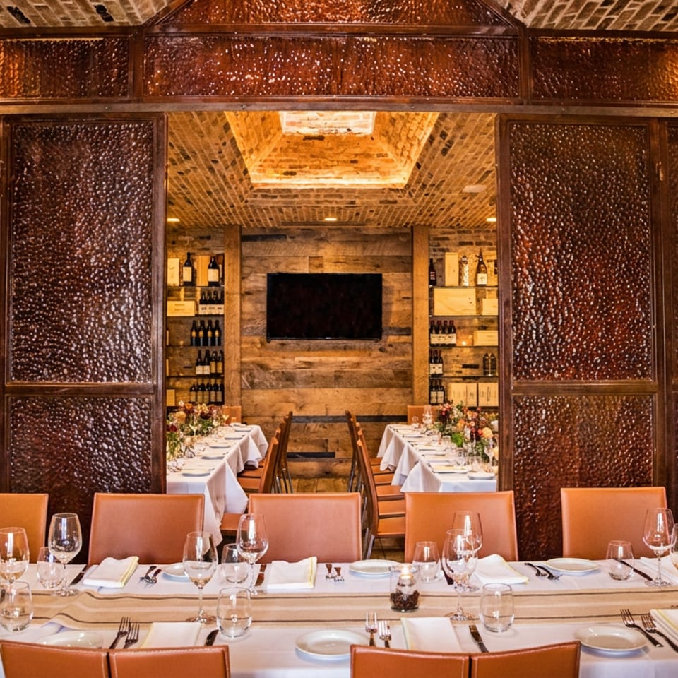 Elegant private dining room with a long set table and open copper doors revealing a wine display.