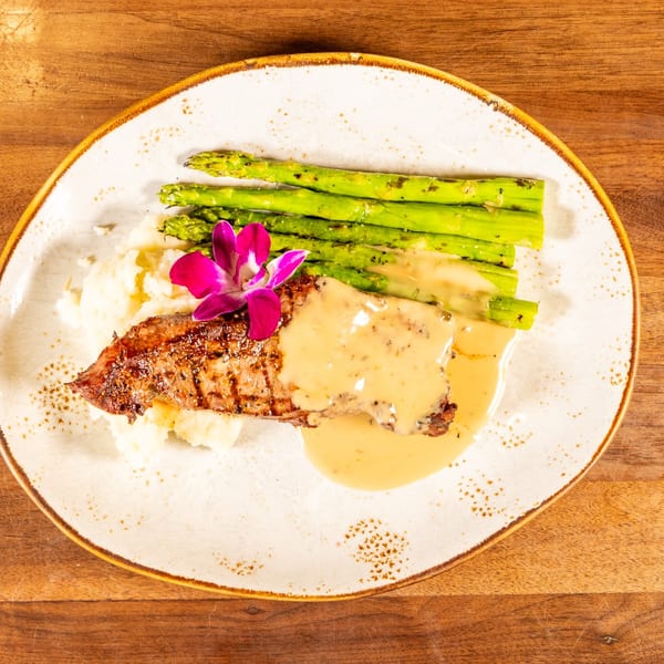 Grilled steak with sauce, mashed potatoes, asparagus, and a purple orchid on a white plate.