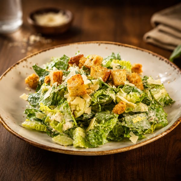 Creamy Caesar salad with romaine lettuce, Parmesan shavings, and golden croutons on a rustic plate.