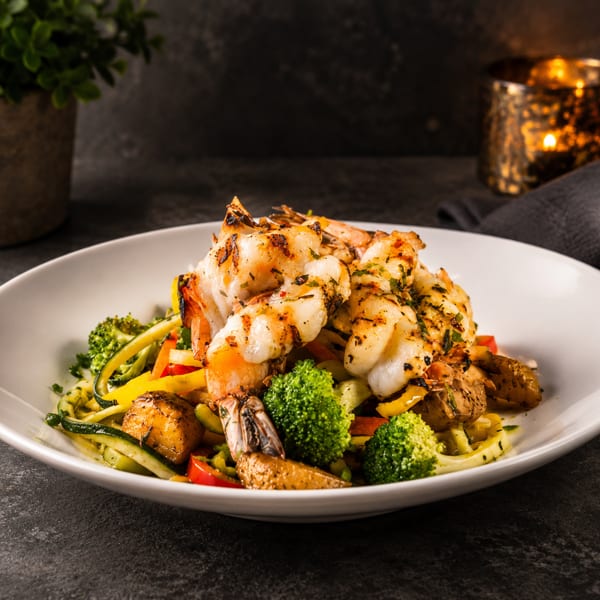 Grilled shrimp and lobster tail served over roasted potatoes, zucchini noodles, broccoli, and colorful peppers.
