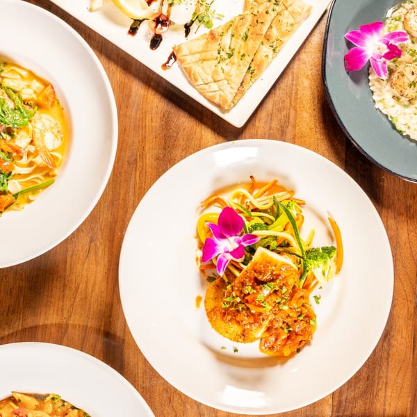 Overhead view of four plates of food, including shrimp pasta, scallops, and fish with vegetables.
