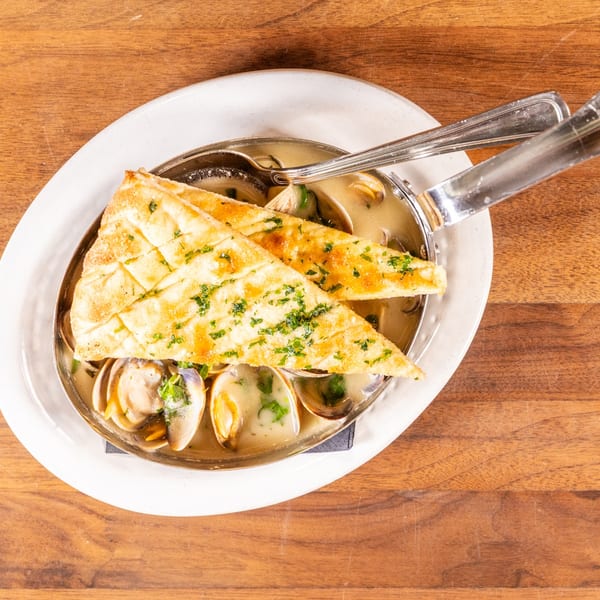 Steamed clams in a creamy broth with fresh herbs, served with two pieces of toasted flatbread.