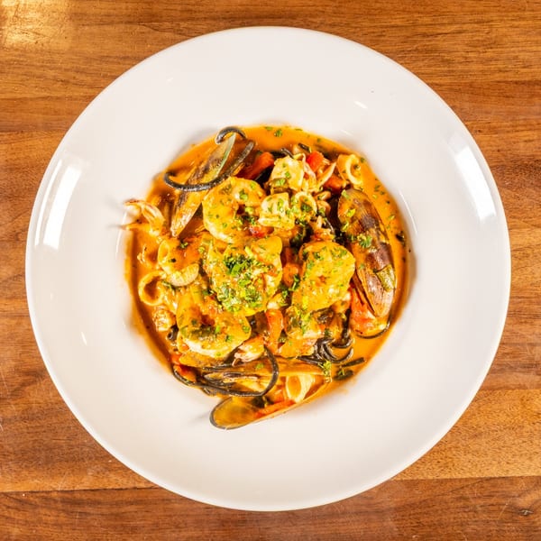 Seafood pasta with shrimp, mussels, and squid in a rich red sauce, garnished with herbs.