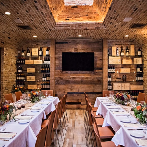 Private dining room with arched brick ceiling, two set tables, and wine bottle displays.