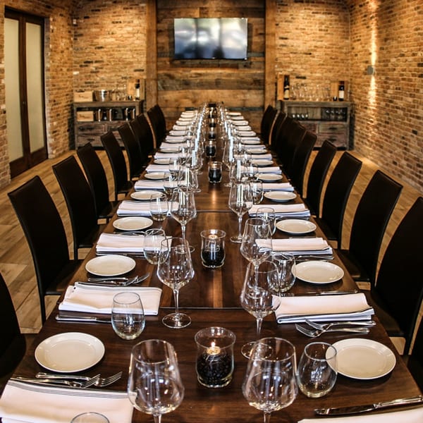 Long dining table set for a private event in a room with brick walls and wine shelves.