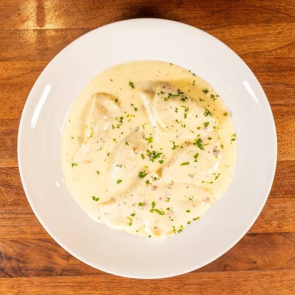 Creamy ravioli dish topped with fresh parsley, served on a white plate on a wooden table.